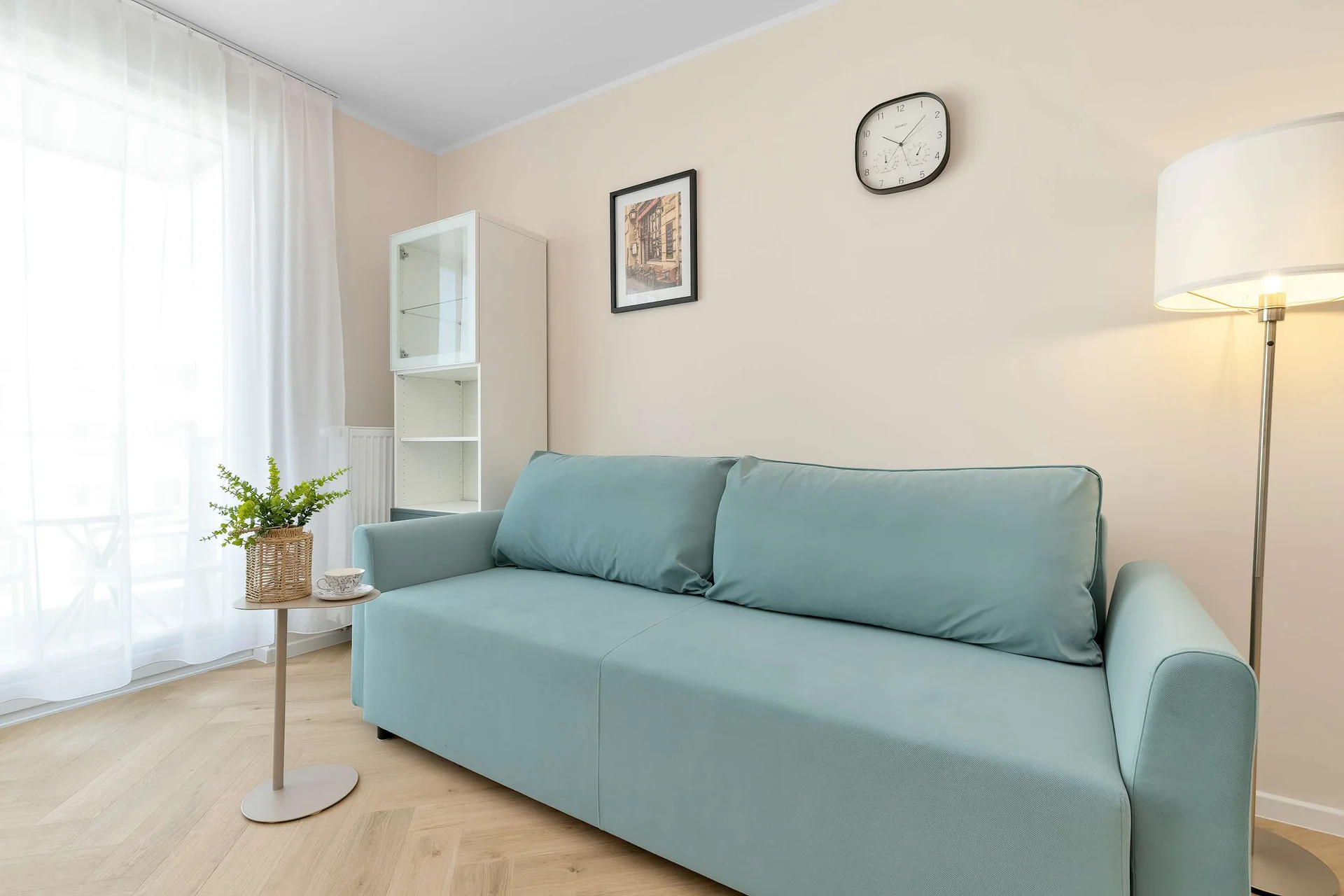 Bright and cozy living room with a comfortable light-blue sofa, a floor lamp and large windows providing plenty of natural light.