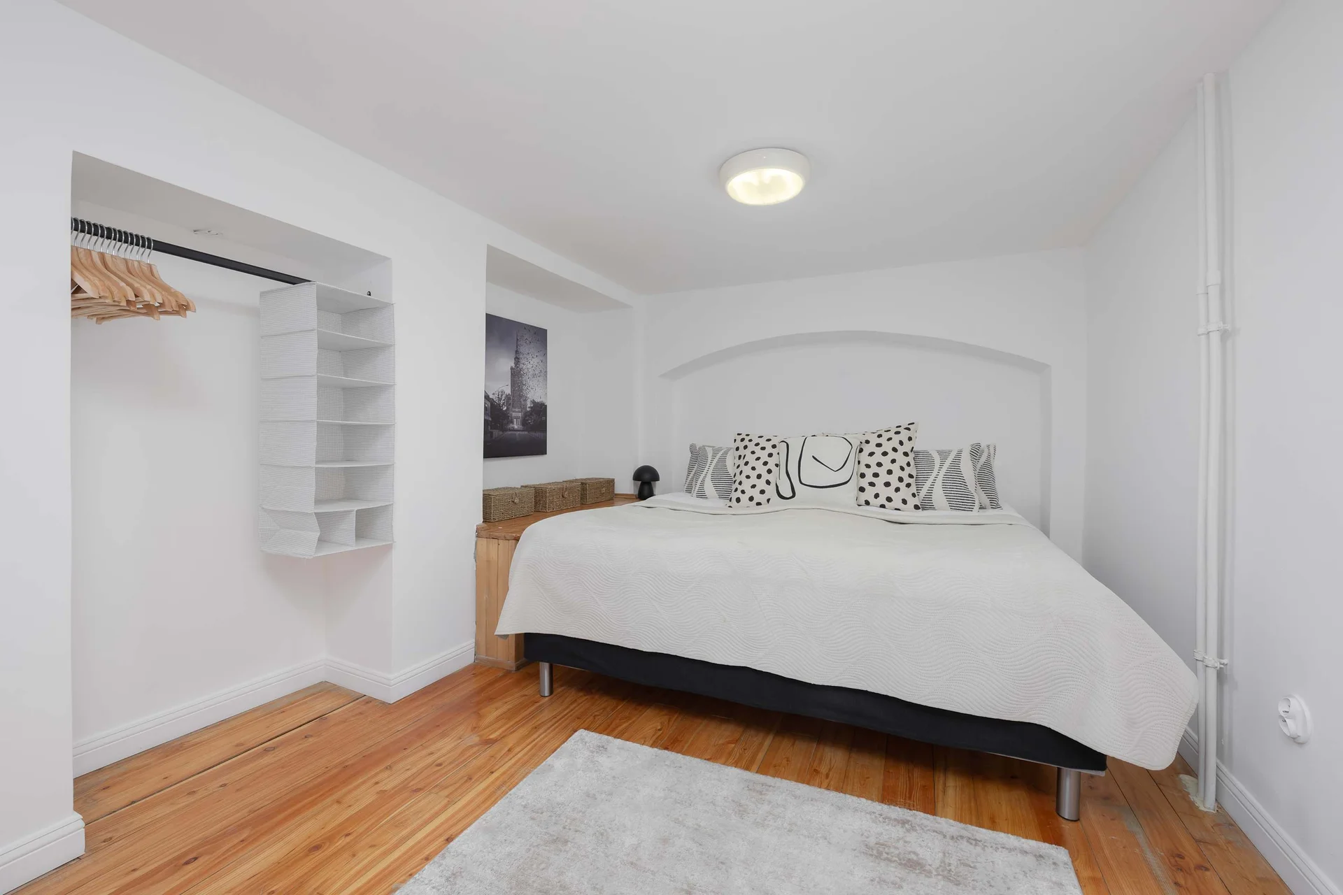 A second bright bedroom with a queen-size bed and clothes hangers.