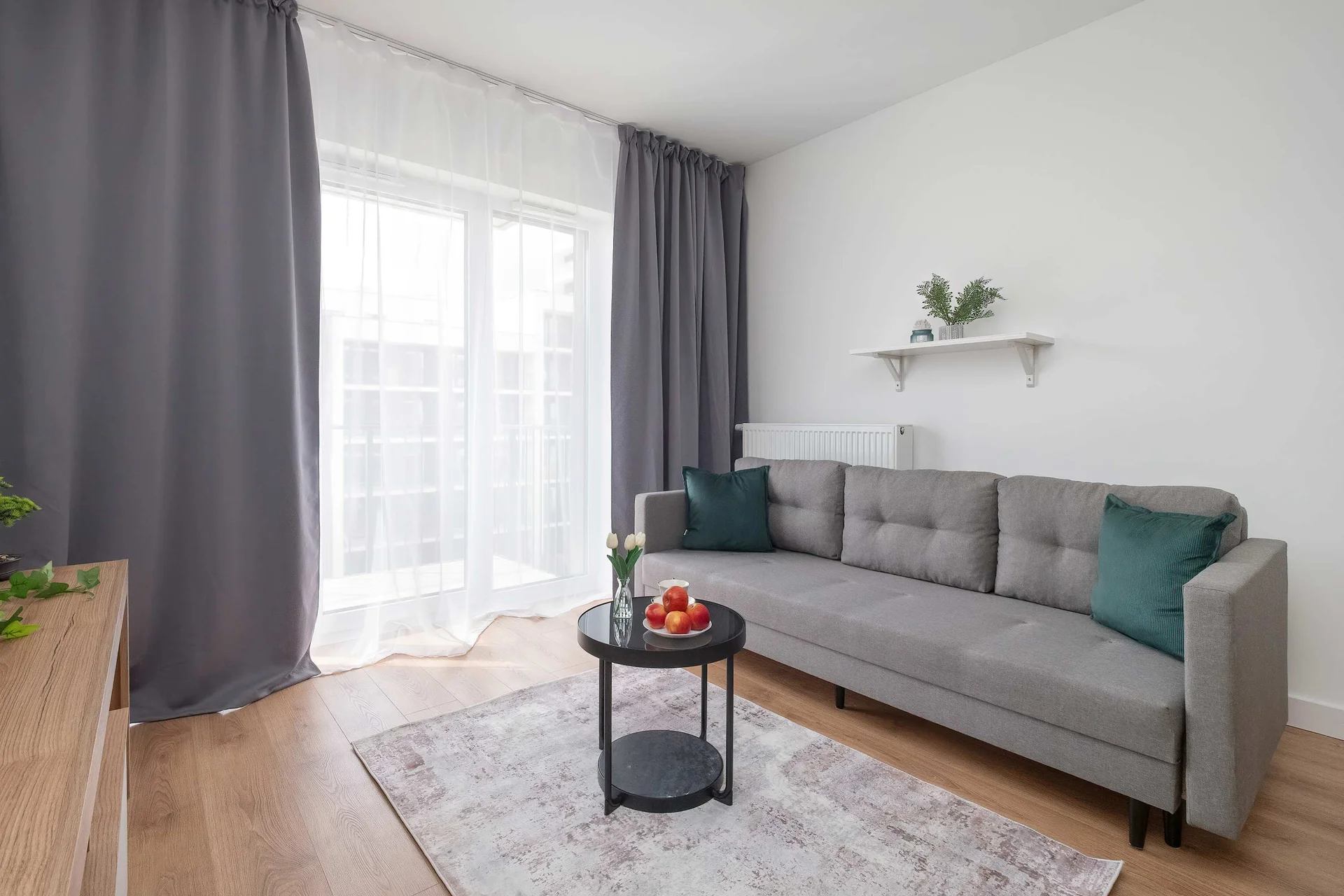 Bright and cozy living room with grey sofa, coffee table, rug, and large windows with grey curtains.
