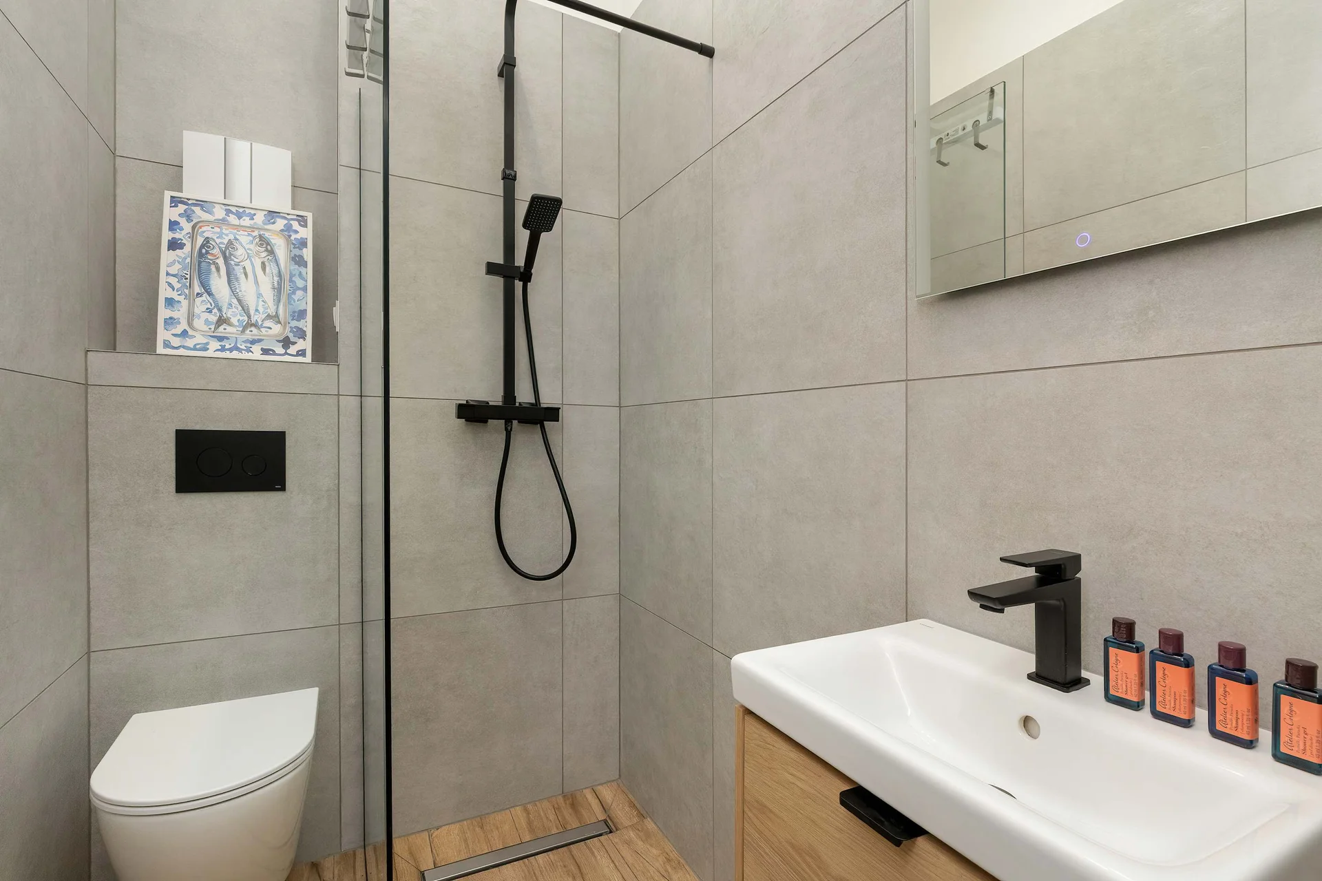 A modern bathroom is lined with neutral stone tiles and includes a glass shower partition, a toilet, and a sleek rectangular sink. Matte black hardware adds a contemporary designer finish to the room.