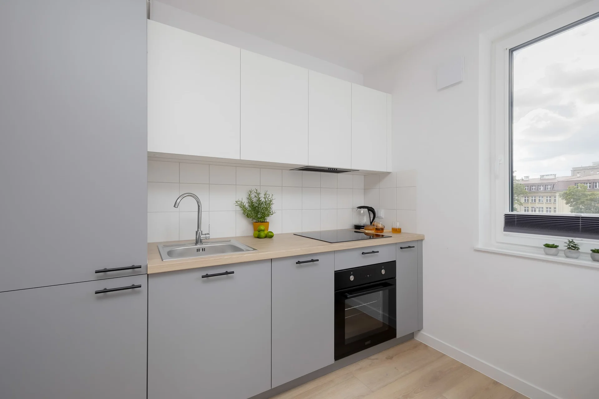 Modern kitchenette with white and grey cabinets, built-in appliances, sink and a large window.