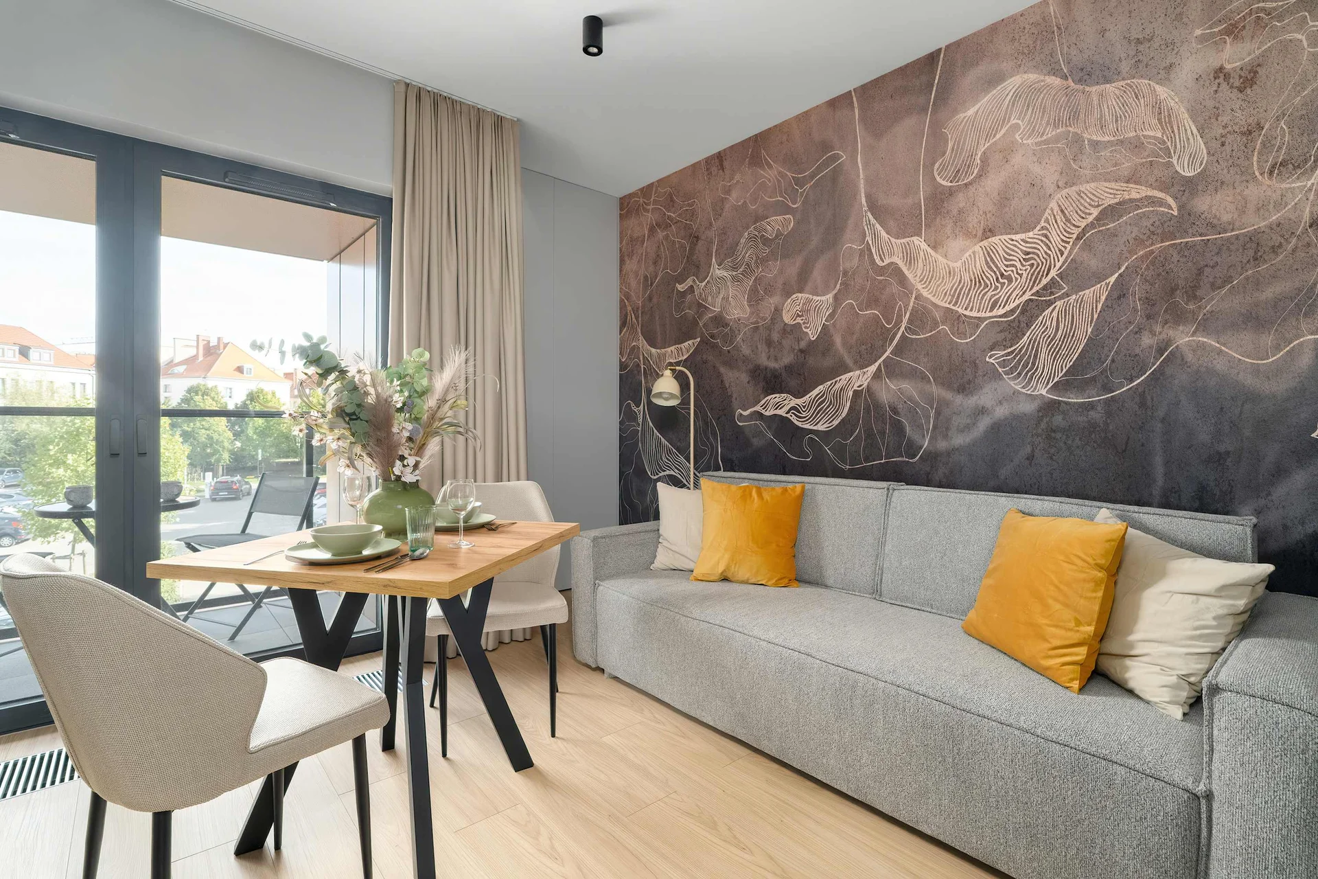 Bright and stylish studio with a grey sofa, dining area, TV and large windows overlooking the surroundings.