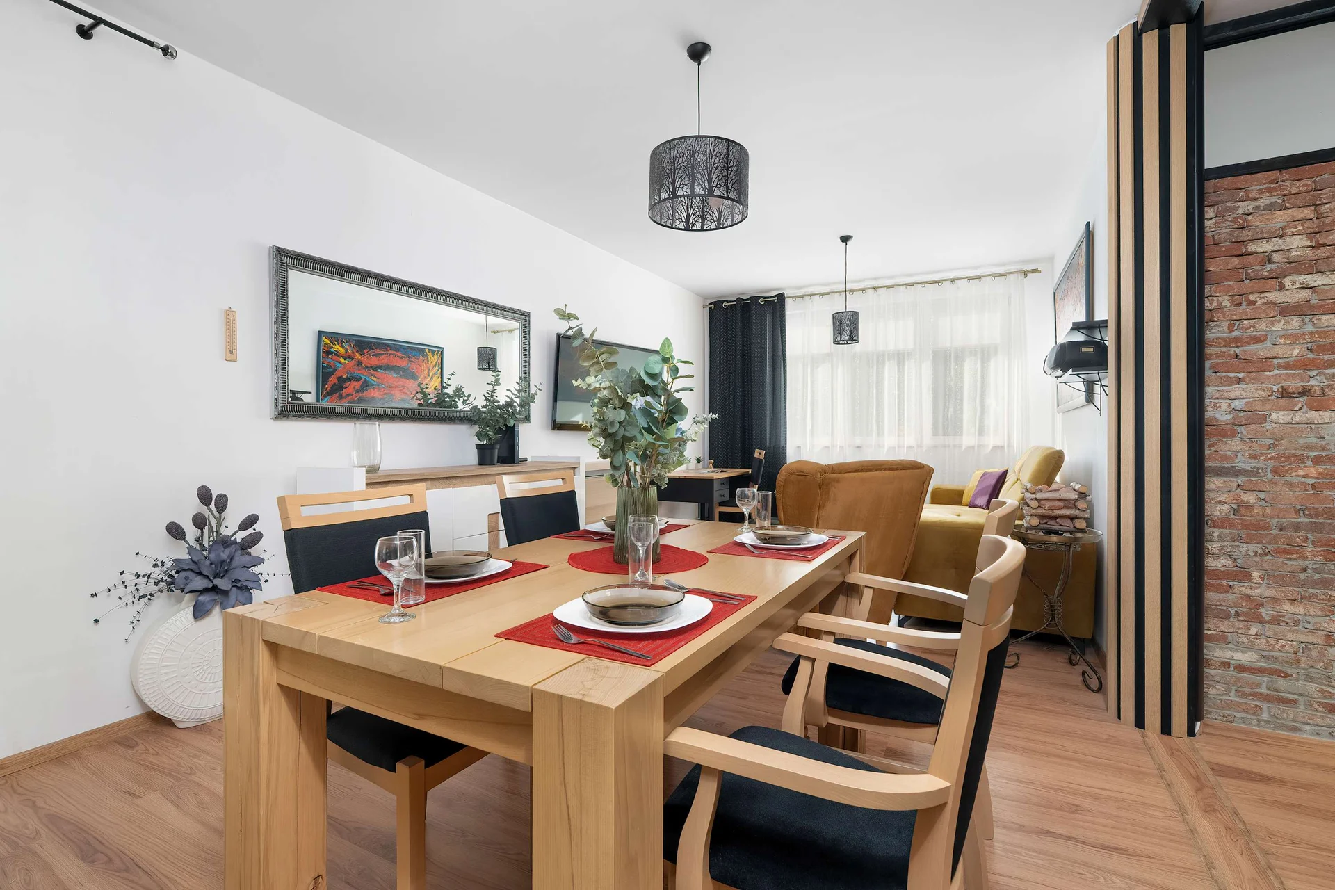 An open dining area with a wooden table, upholstered chairs, colorful artwork, and a view toward the kitchen.