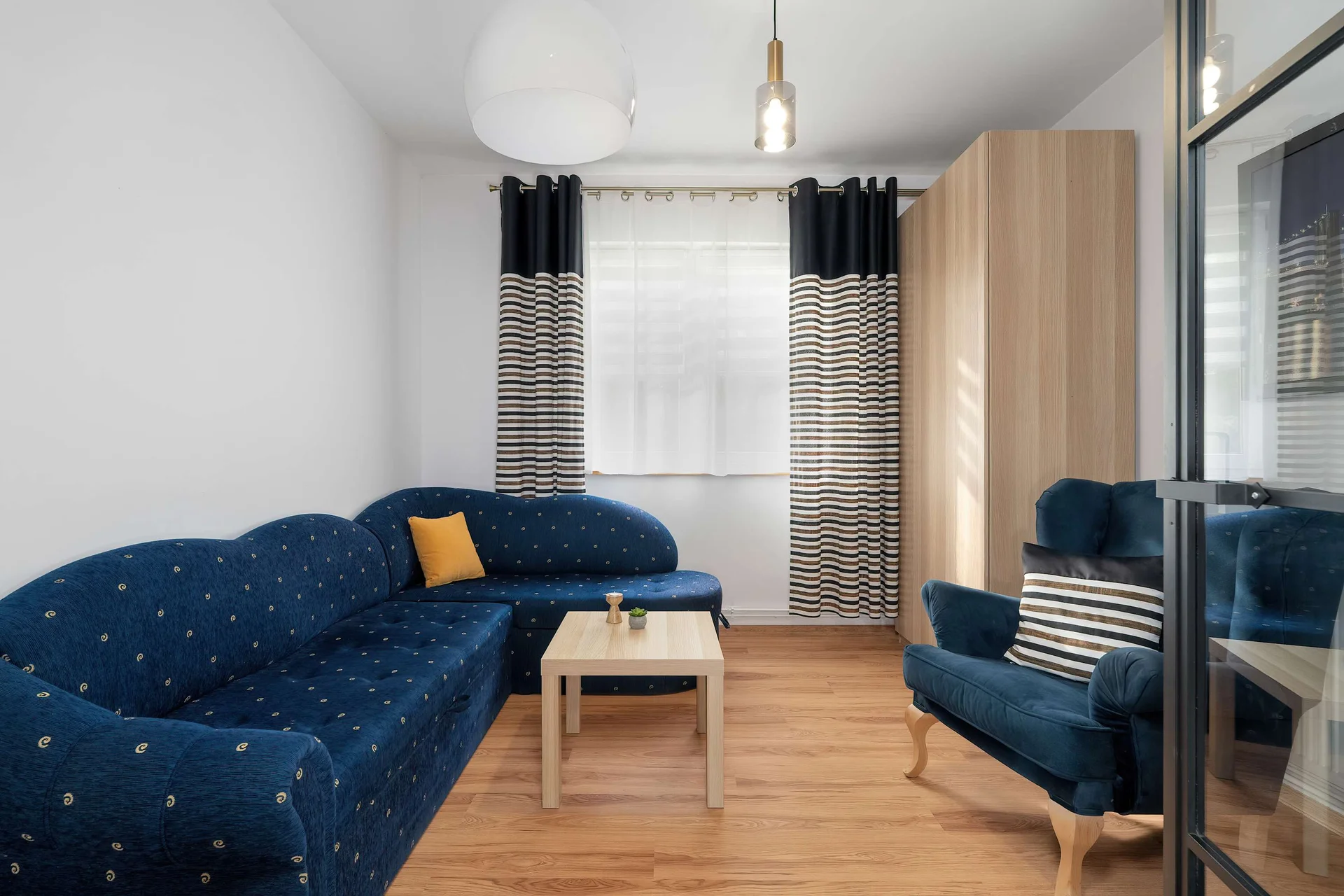 A comfortable lounge with a deep blue sofa, mustard cushions, and large windows dressed with dark curtains.