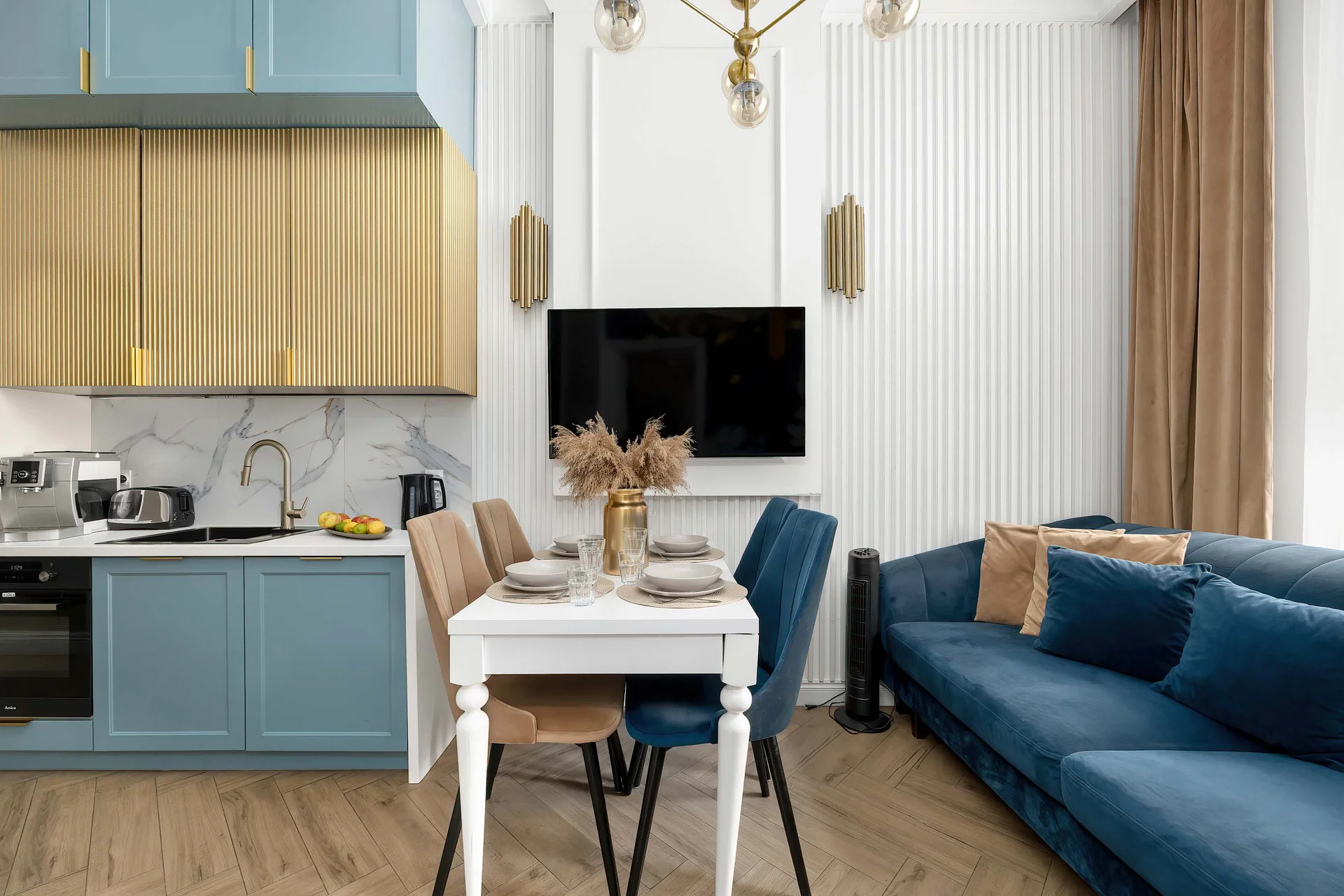 A stylish living area with a blue sofa, a dining table, and a modern kitchen in the background. The elegant furniture and carefully chosen colors make the apartment feel both comfortable and inviting.