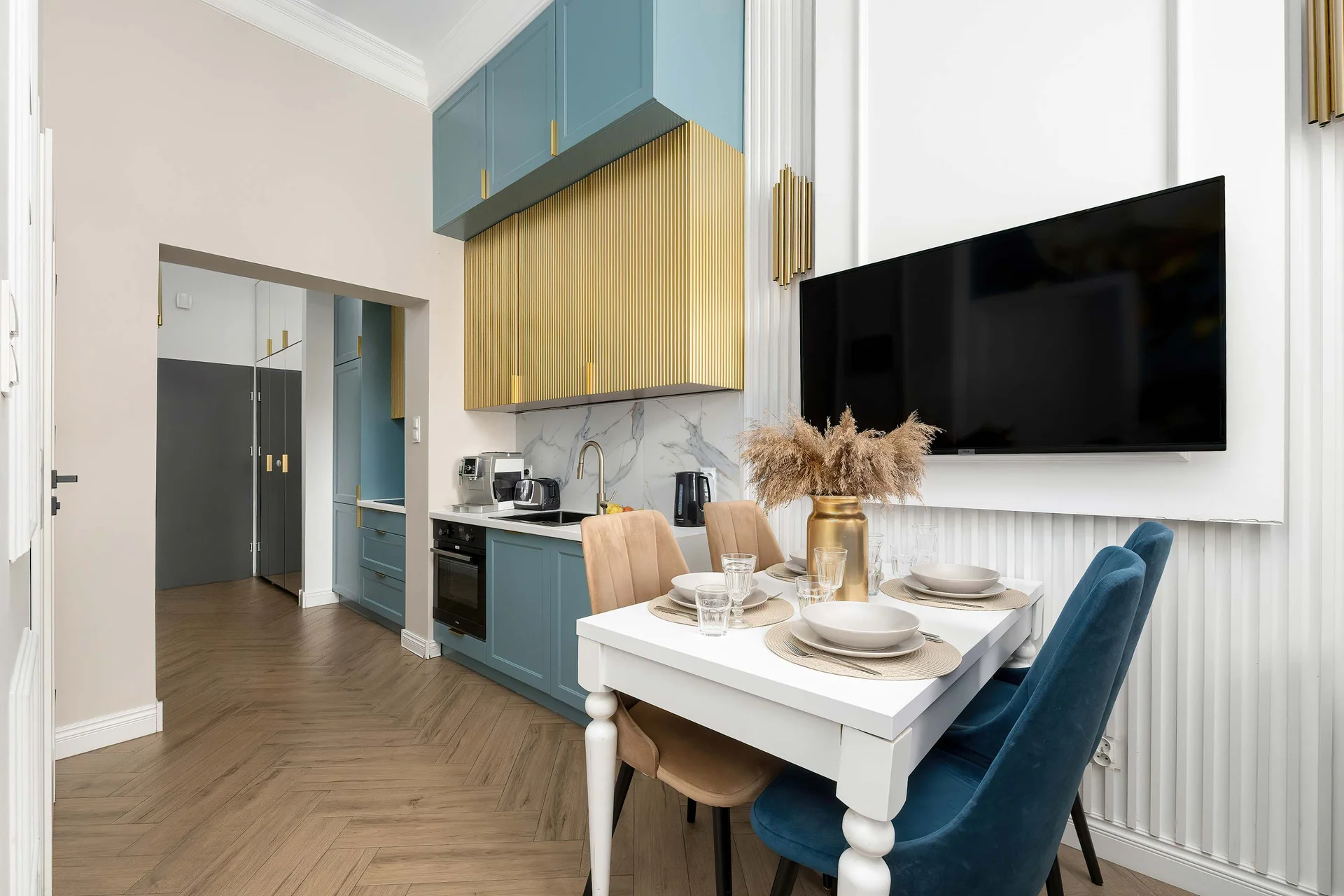 A modern open-plan kitchen featuring blue cabinets, wooden accents, and a stylish dining table. The combination of white walls and warm wooden details gives the space a fresh and sophisticated look.