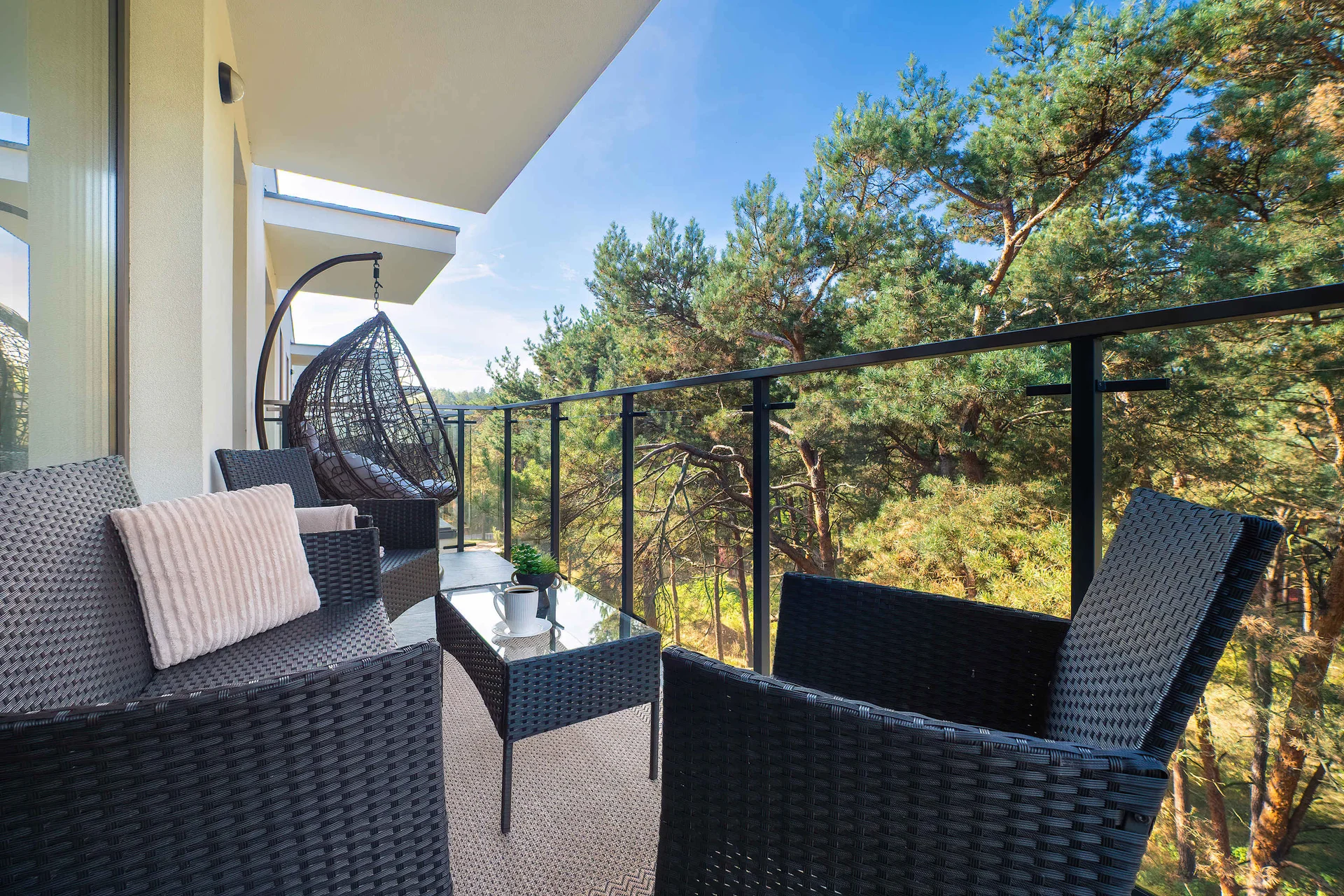 Balcony with black woven outdoor chairs, a small table and views of surrounding greenery.