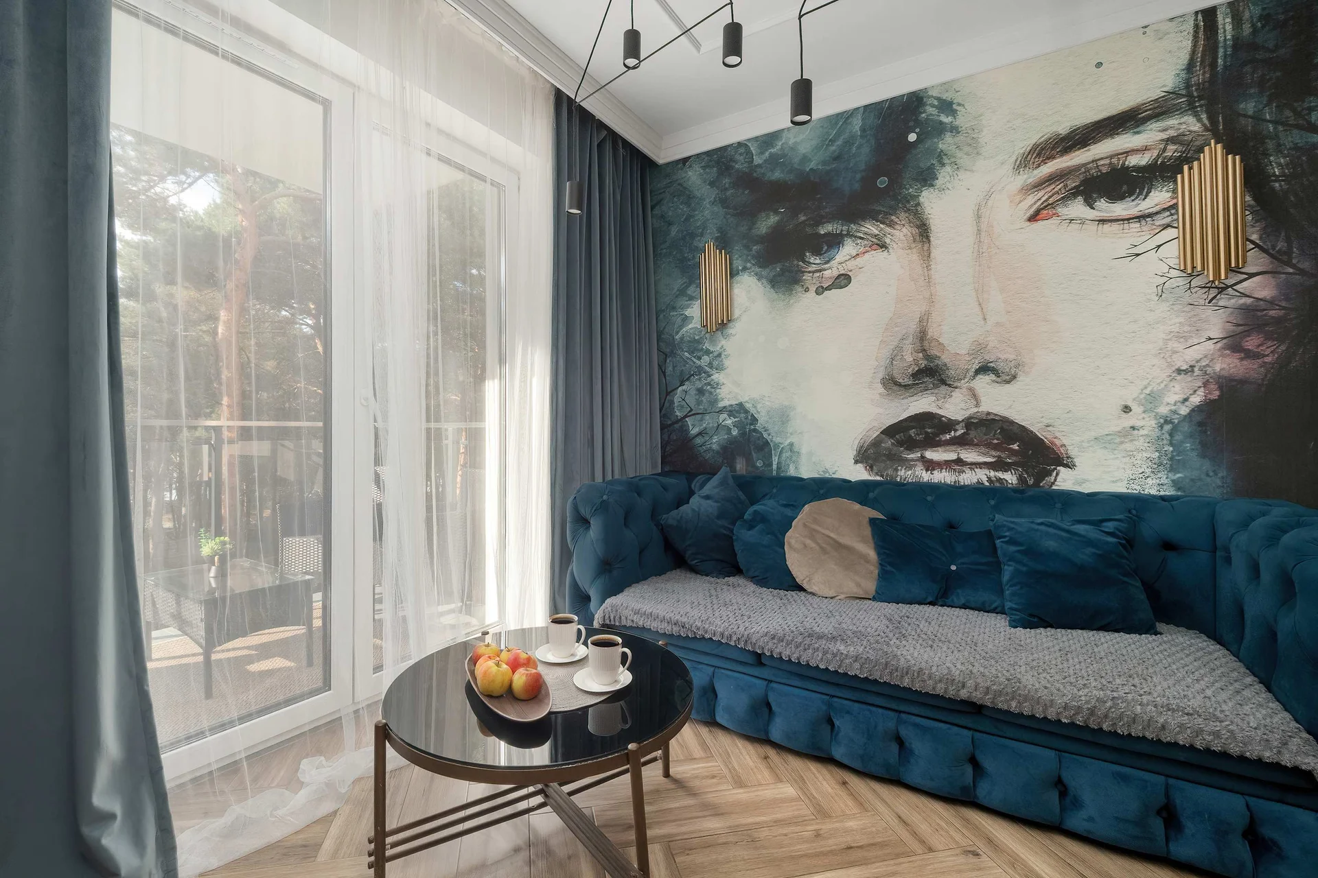 Stylish living room with a blue velvet sofa, large windows, and striking wall art.
