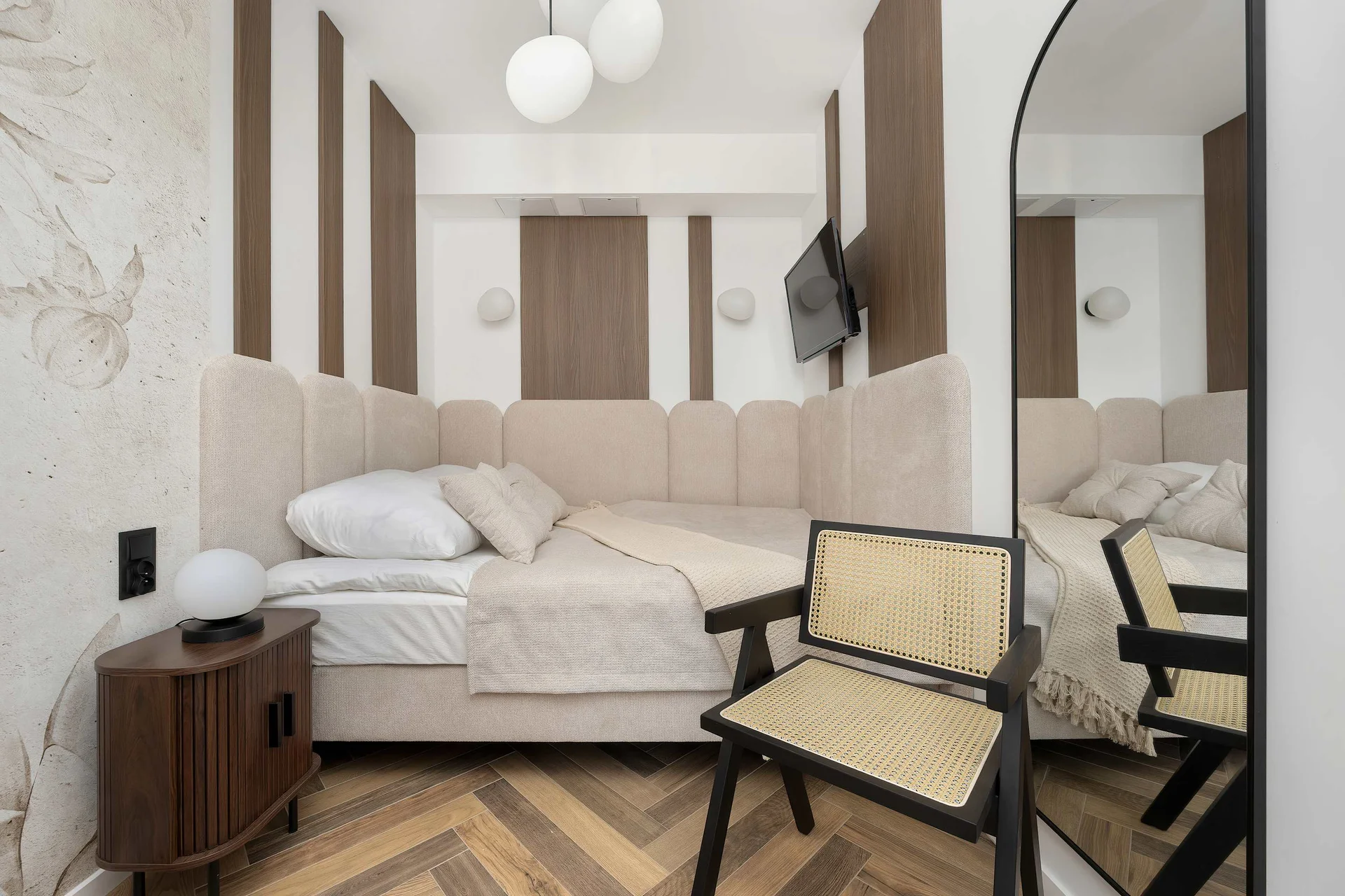 A cozy bedroom with a double bed dressed in crisp white bedding and soft neutral cushions. Two elegant armchairs and warm wooden flooring complement the refined interior.