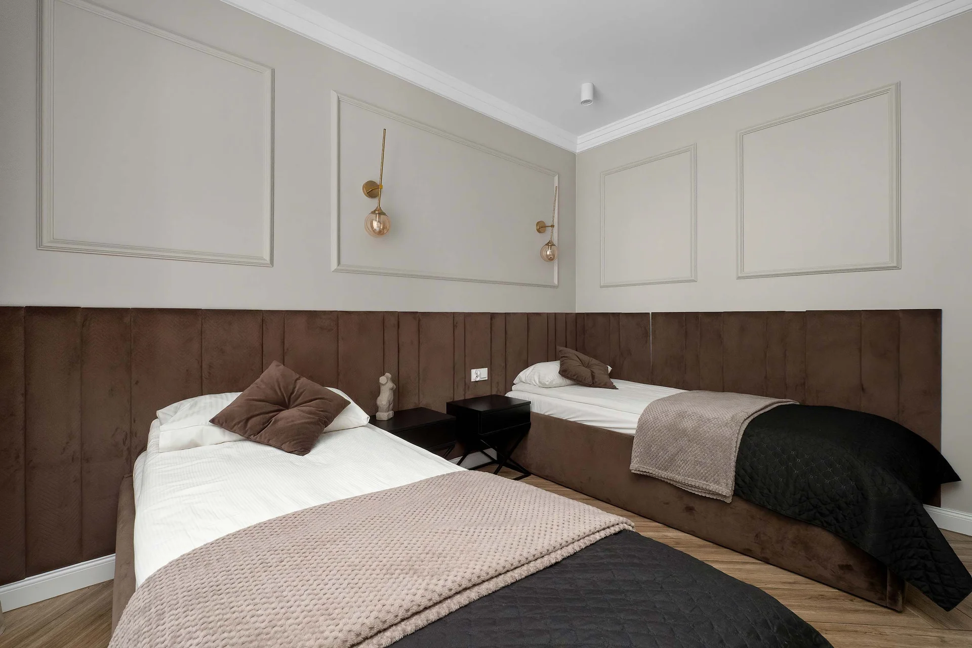 A neutral-toned third bedroom features two single beds with dark throws and white linens. Light beige walls with decorative molding complete the space.