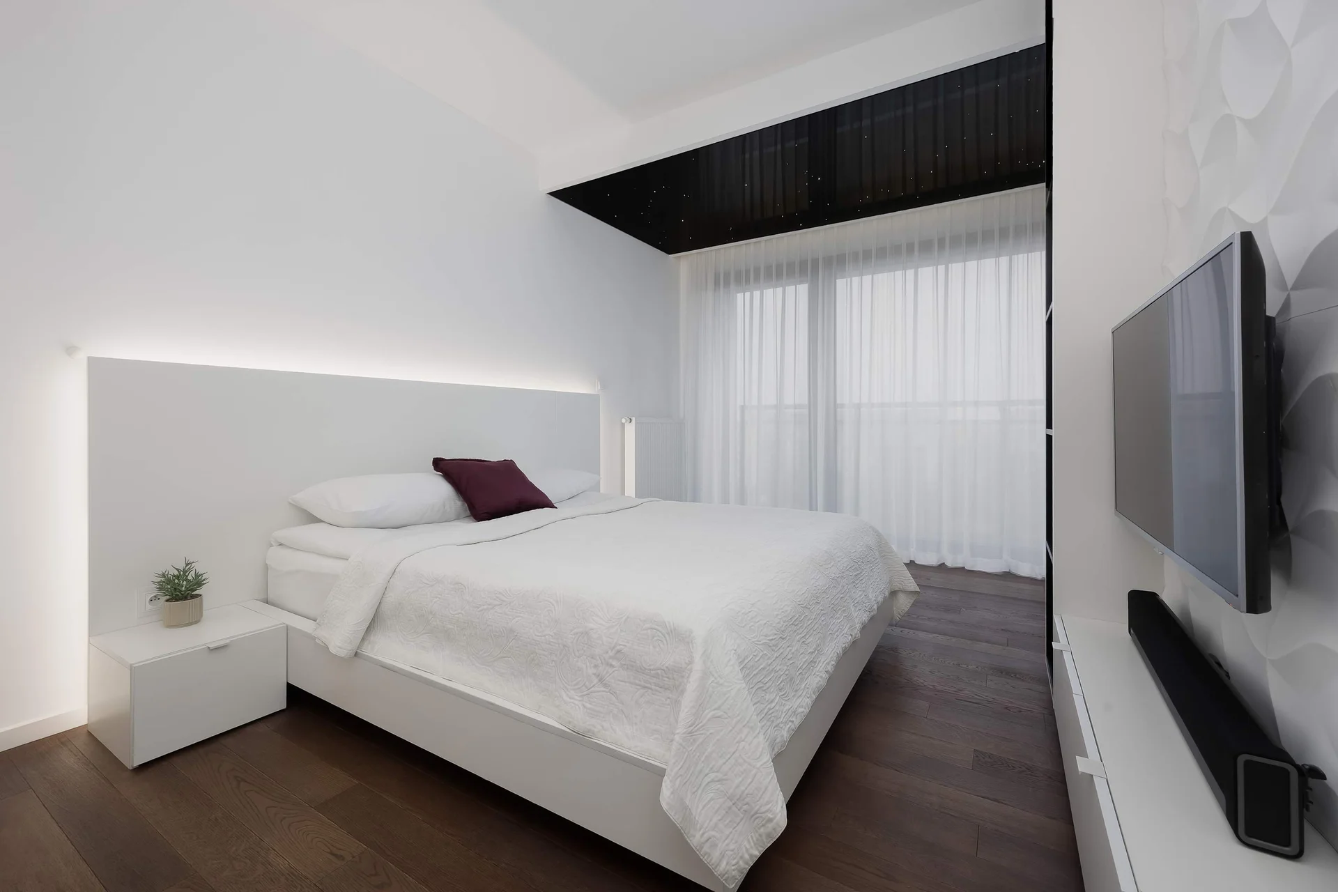 Modern bedroom with a white bed, neutral bedding, a bedside table, and floor-to-ceiling curtains.