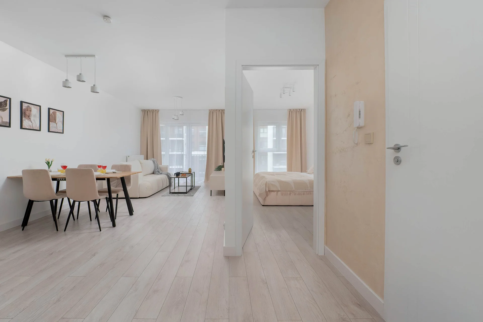 A spacious, bright interior with a dining area, light wooden flooring, and a bedroom visible in the background.