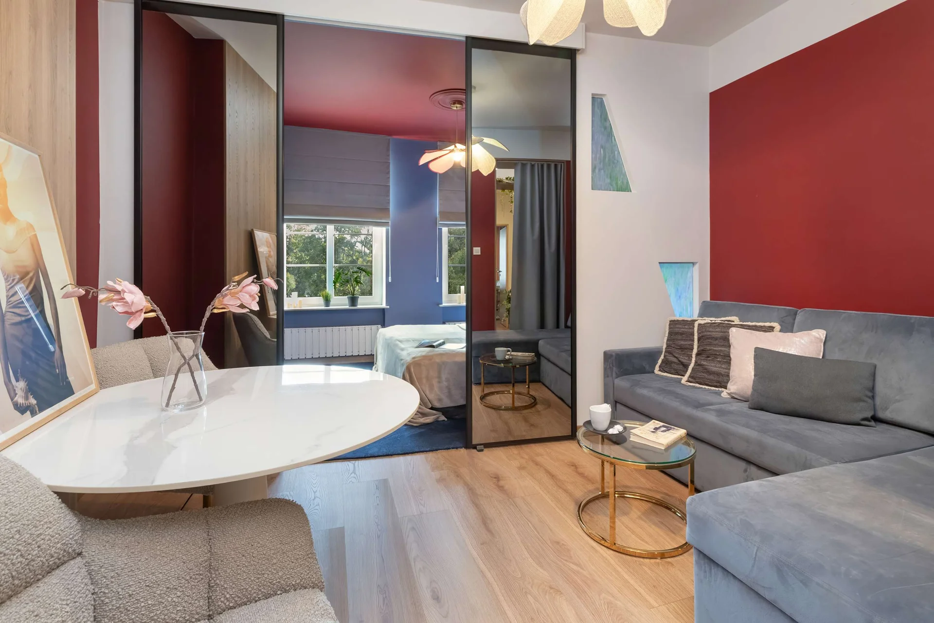 The second seating area features a grey corner sofa set against a deep red accent wall. A round white table with chairs sits nearby under modern lighting.