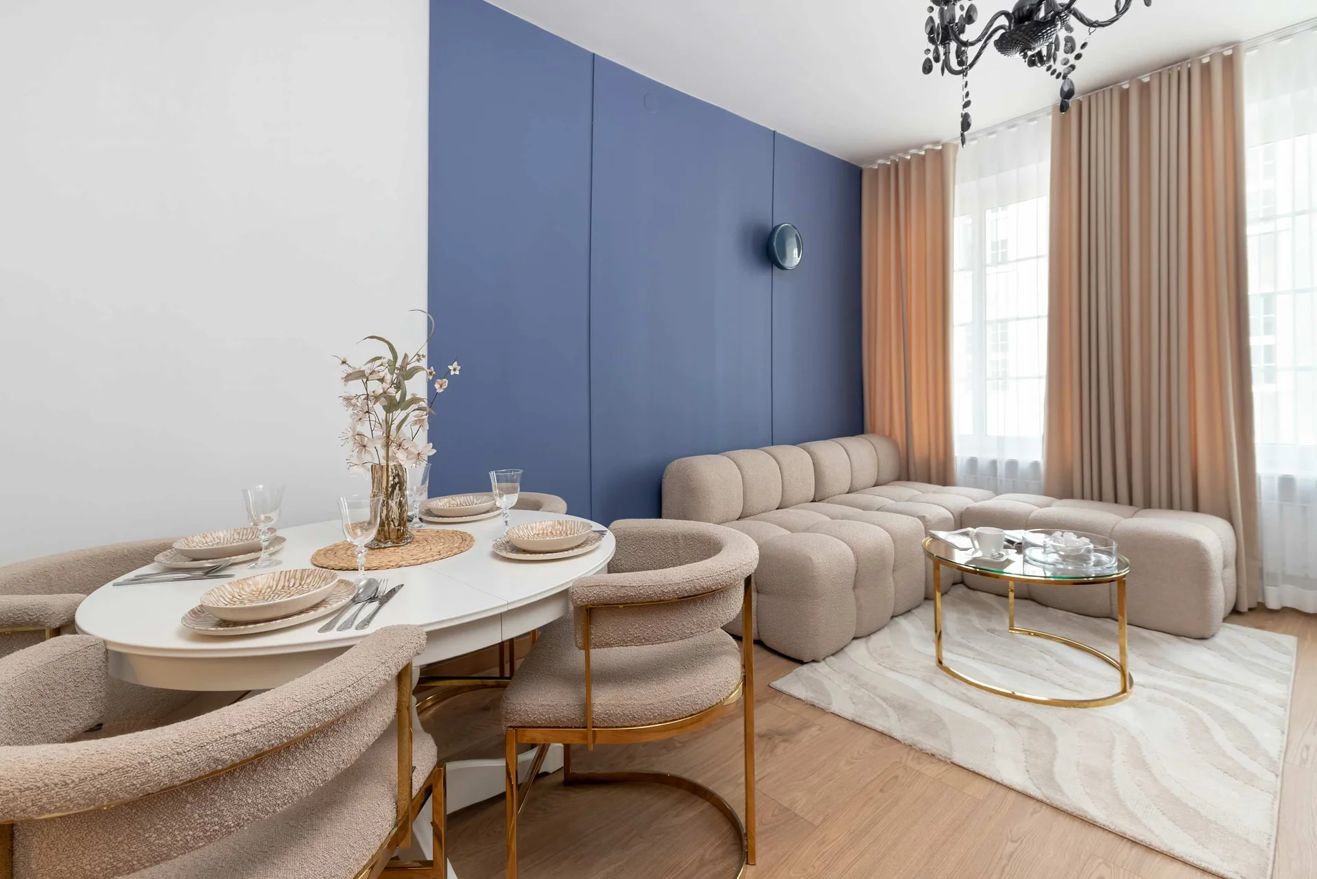The open dining area features a round white table with beige upholstered chairs. The beige sectional sofa and glass coffee table frame the background.