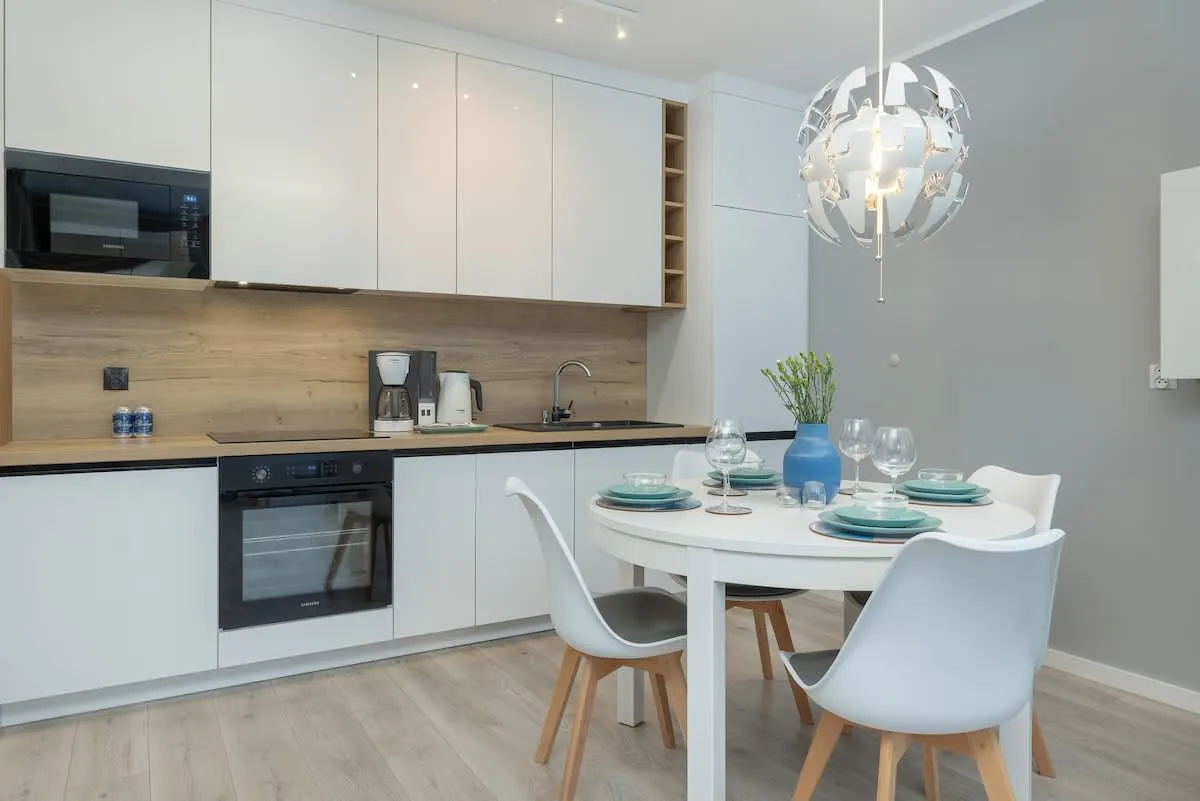 A modern kitchen with white cabinets, wooden accents, and a round dining table.
