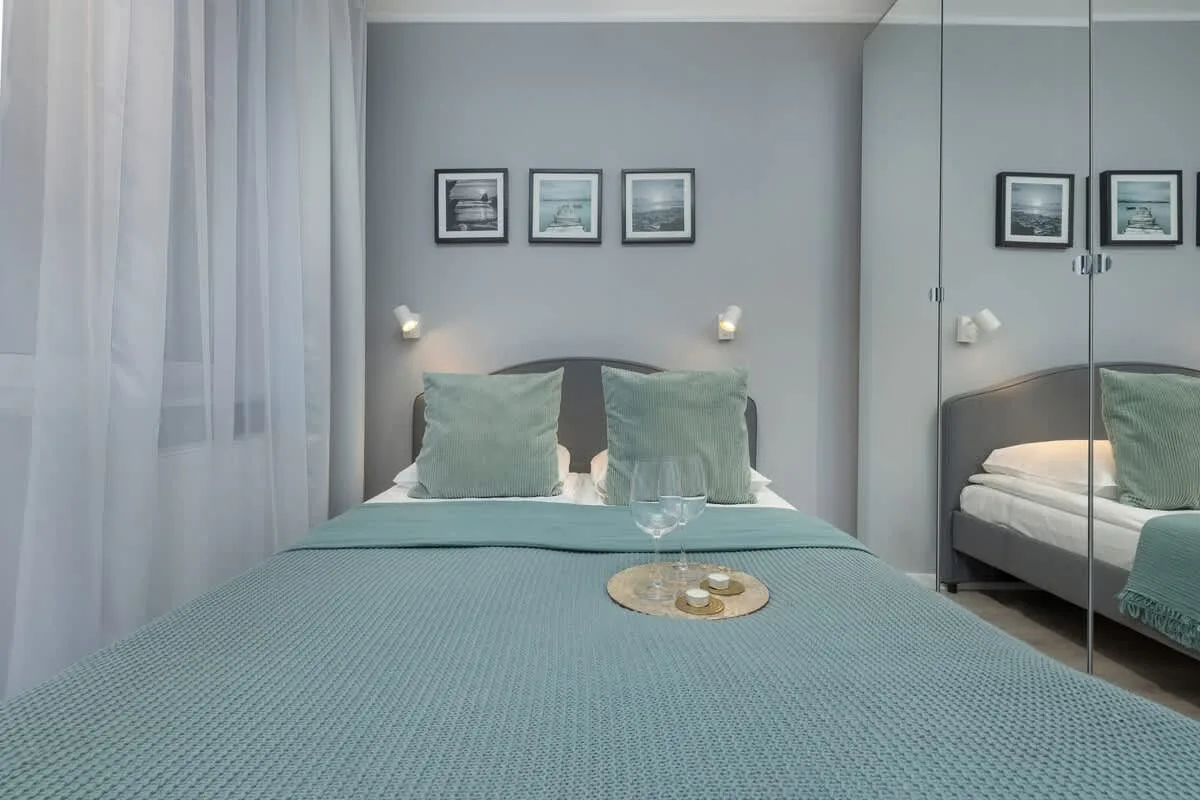 A cozy bedroom with a teal bedspread, decorative pillows, and framed artwork above the bed.