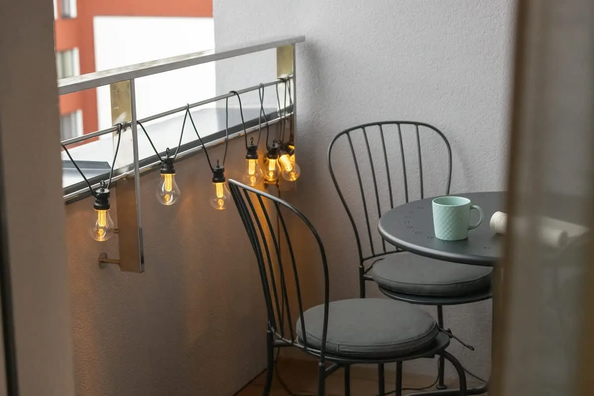 A small balcony with string lights, a round table, and two metal chairs.