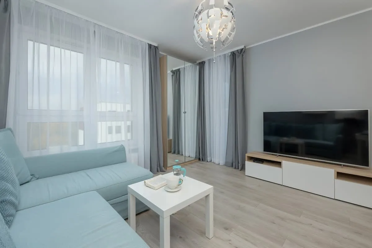 A bright living room with a light blue sofa, a white coffee table, and a flat-screen TV.