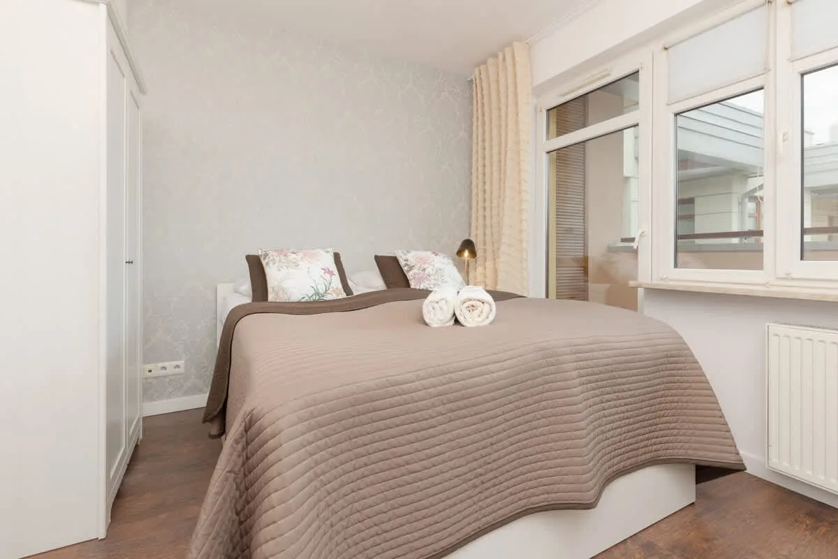 A cozy bedroom featuring a double bed with brown bedding, large windows, and soft lighting.
