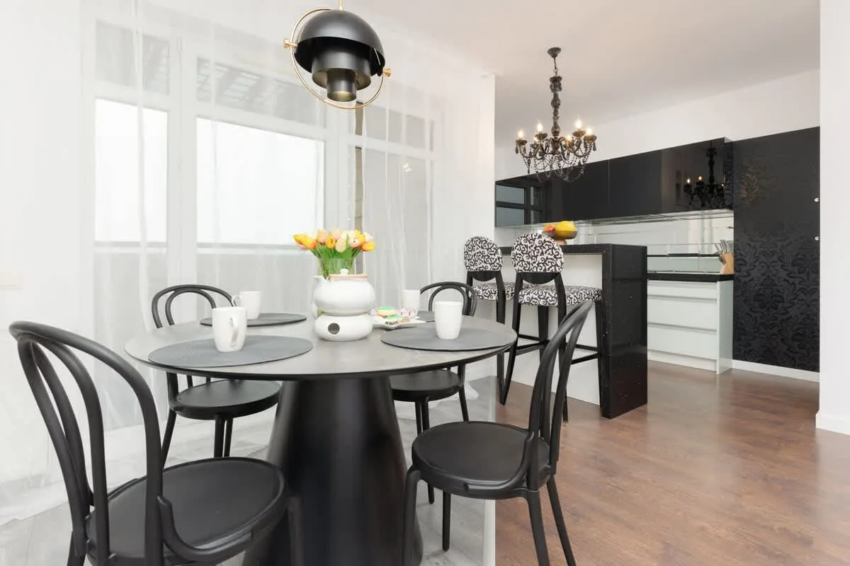 A modern dining area with black chairs, a round table, and bright natural light from large windows.