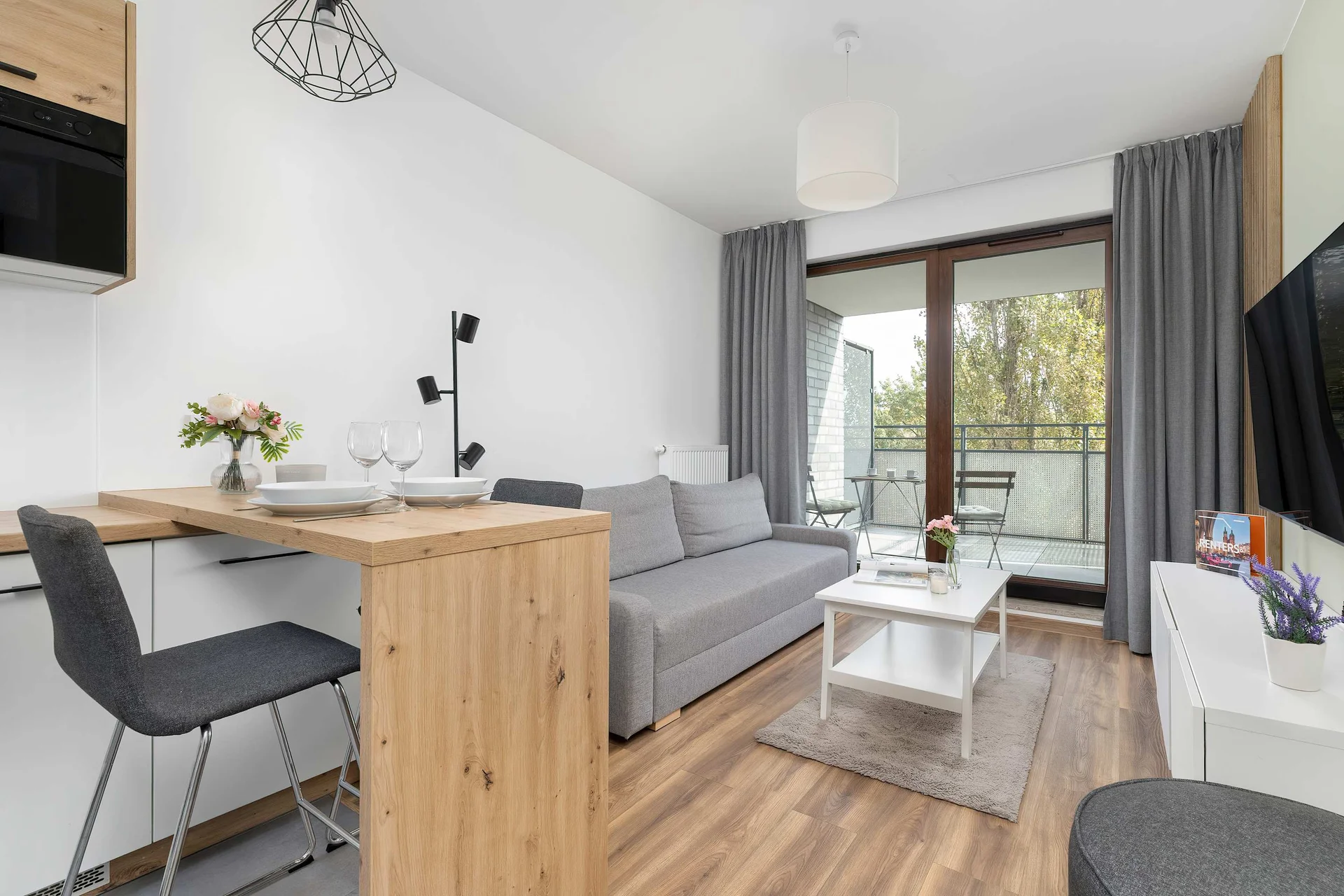 Bright living room with a kitchenette invites relaxation, offering a comfortable sofa, natural light, and a view of the greenery outside.