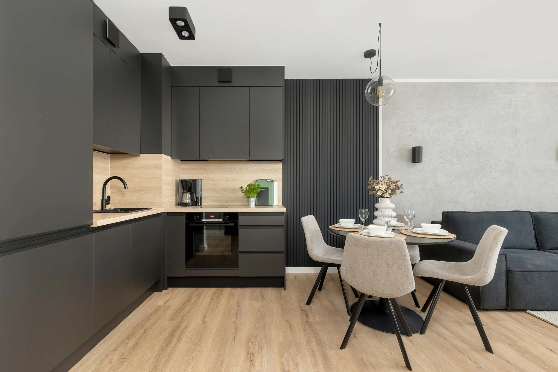 A modern open-plan kitchenette and dining area with black cabinetry, wooden accents, and a round table with four chairs.