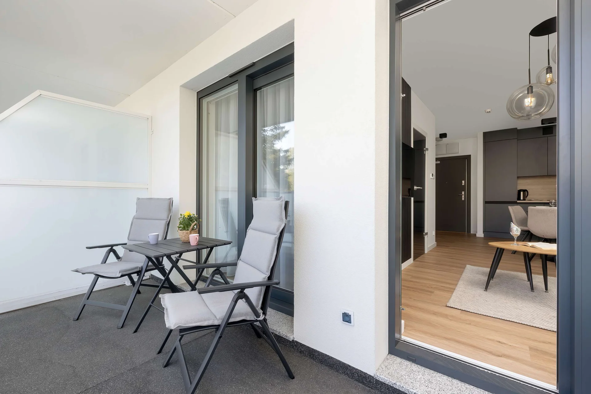 A furnished balcony with a glass railing, two chairs, and a small table, offering an inviting space to enjoy the outdoors.