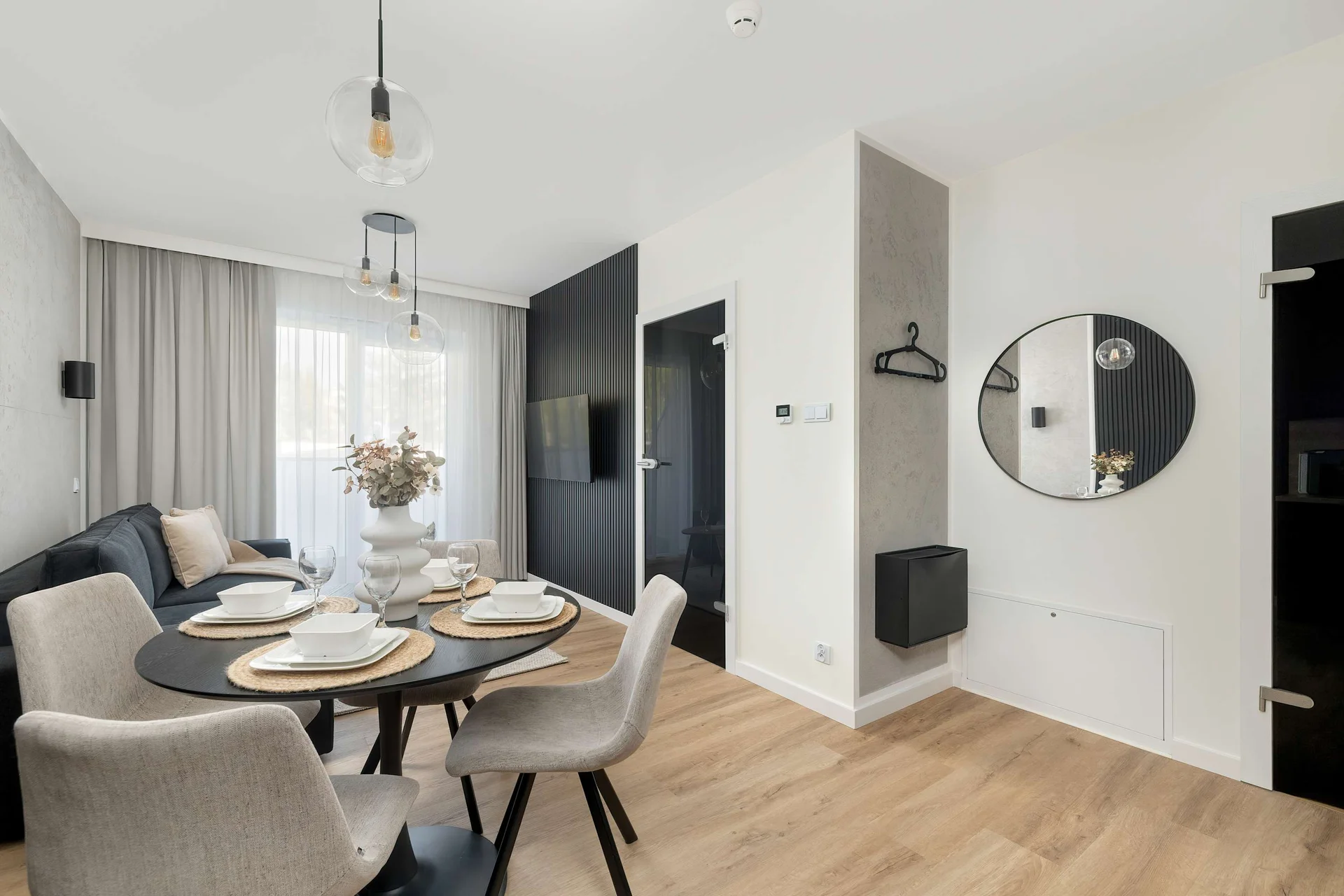 An entryway view into a bright, open-plan living and dining area, accented by a large mirror and elegant lighting.