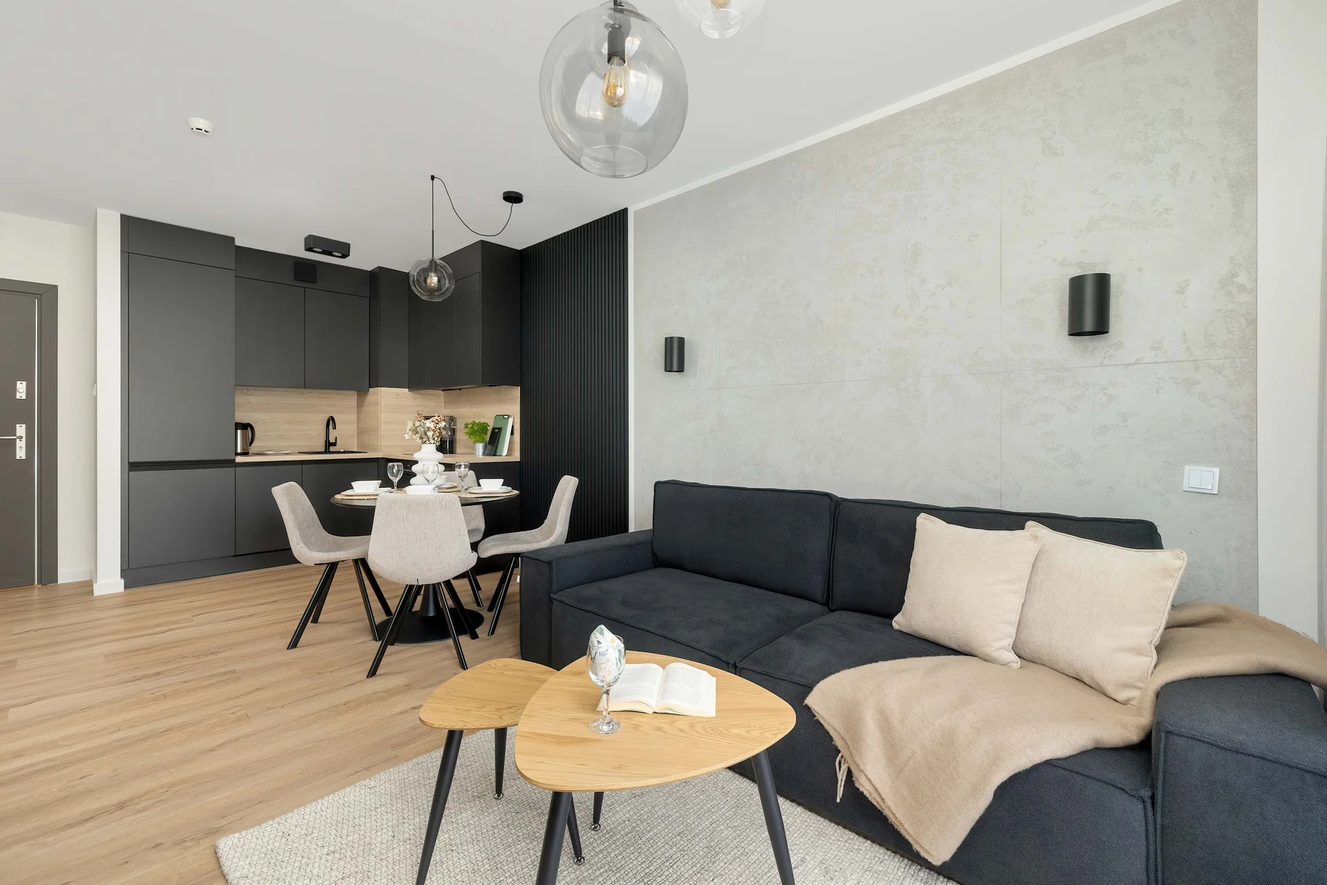 A stylish living room with a dark sectional sofa, round nesting tables, and a mounted TV, complemented by minimalist decor.