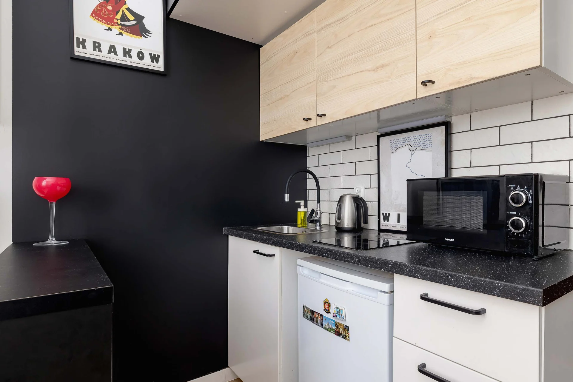 A modern kitchenette with bright cabinetry and a contrasting black wall, equipped with the necessary appliances.