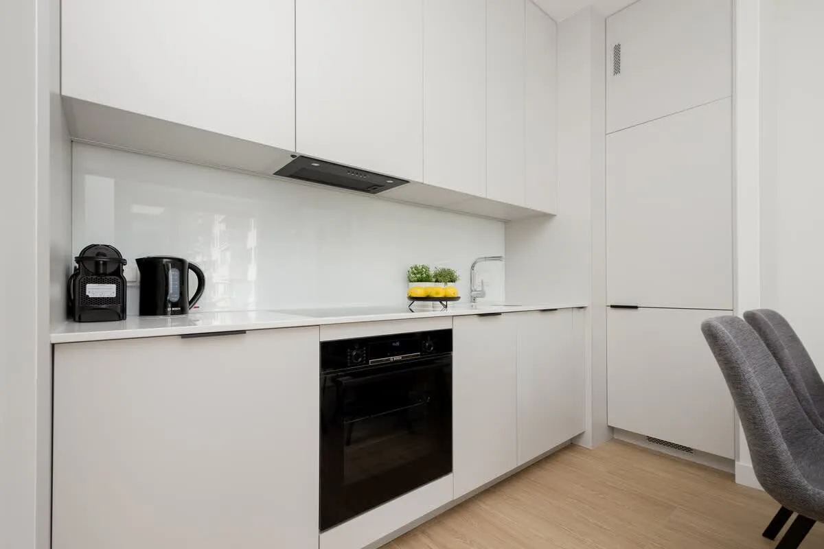 A minimalist kitchen with white cabinets, a built-in oven, and small appliances like a kettle and coffee maker.