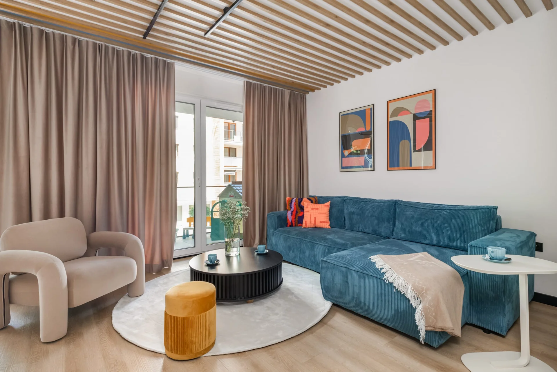 Spacious living area with a teal sofa, modern coffee table, and wooden ceiling accents.
