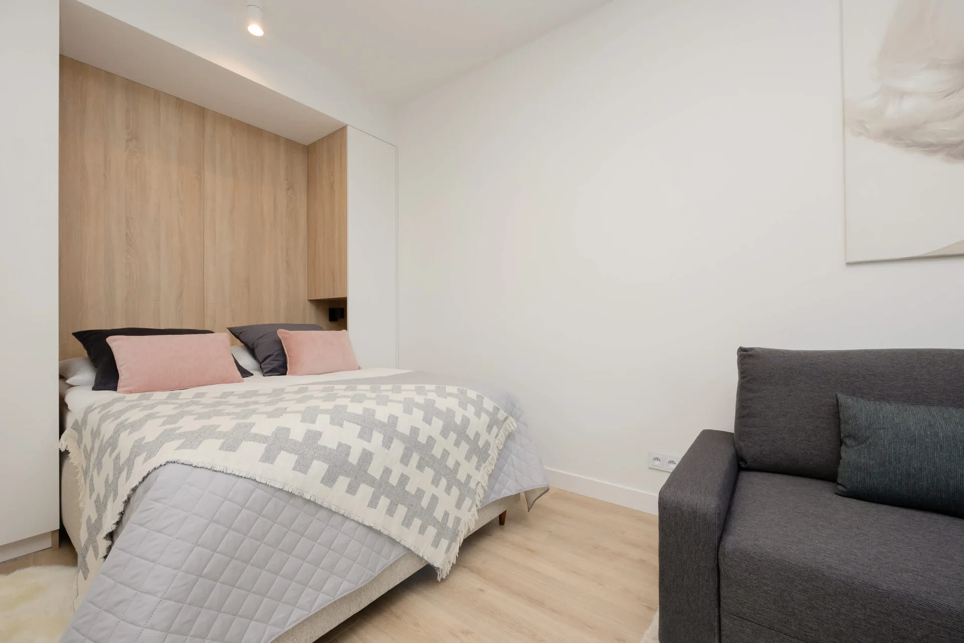 A cozy bedroom corner with a built-in wooden headboard, soft lighting, and stylish gray and pink bedding.
