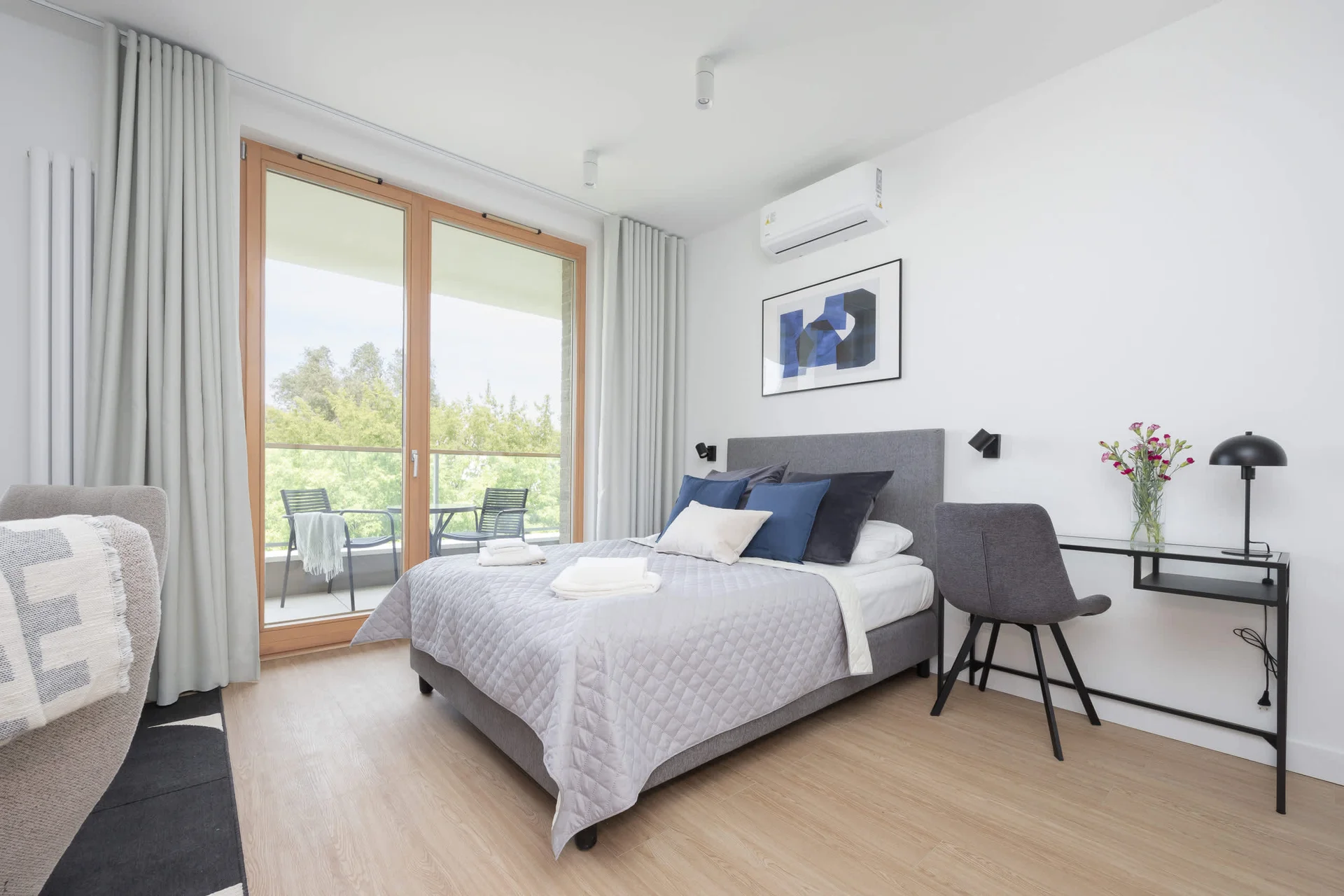 A bedroom with a soft green throw blanket and a large window letting in ample daylight.
