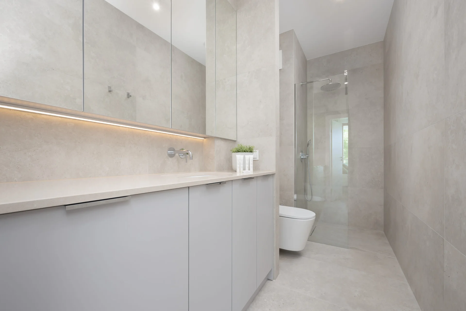 A sleek bathroom with a minimalist design, featuring a wall-mounted toilet, light tiles, and wood accents.