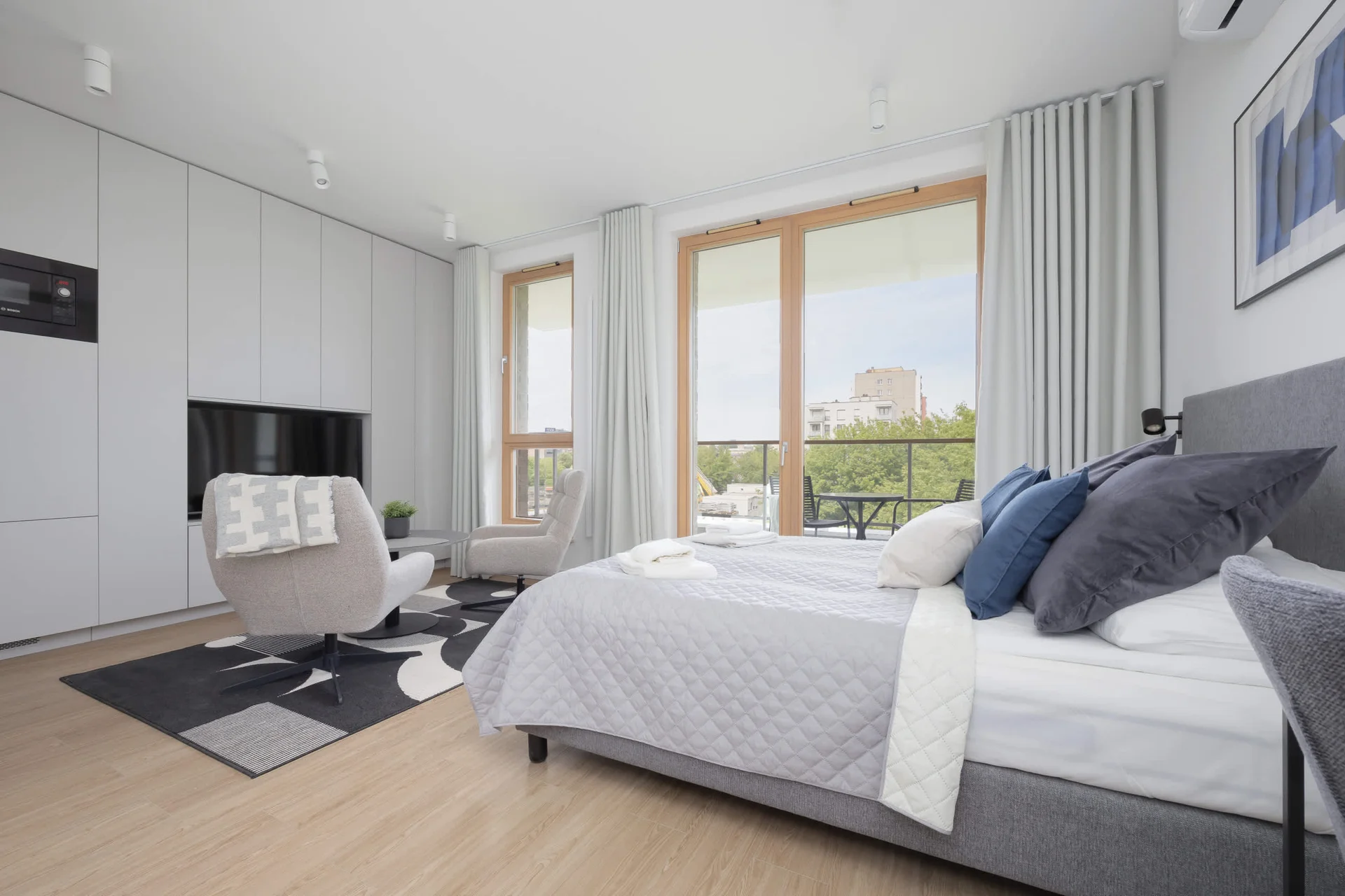 A stylish living space with modern furnishings, wooden flooring, and a bright atmosphere from large windows.