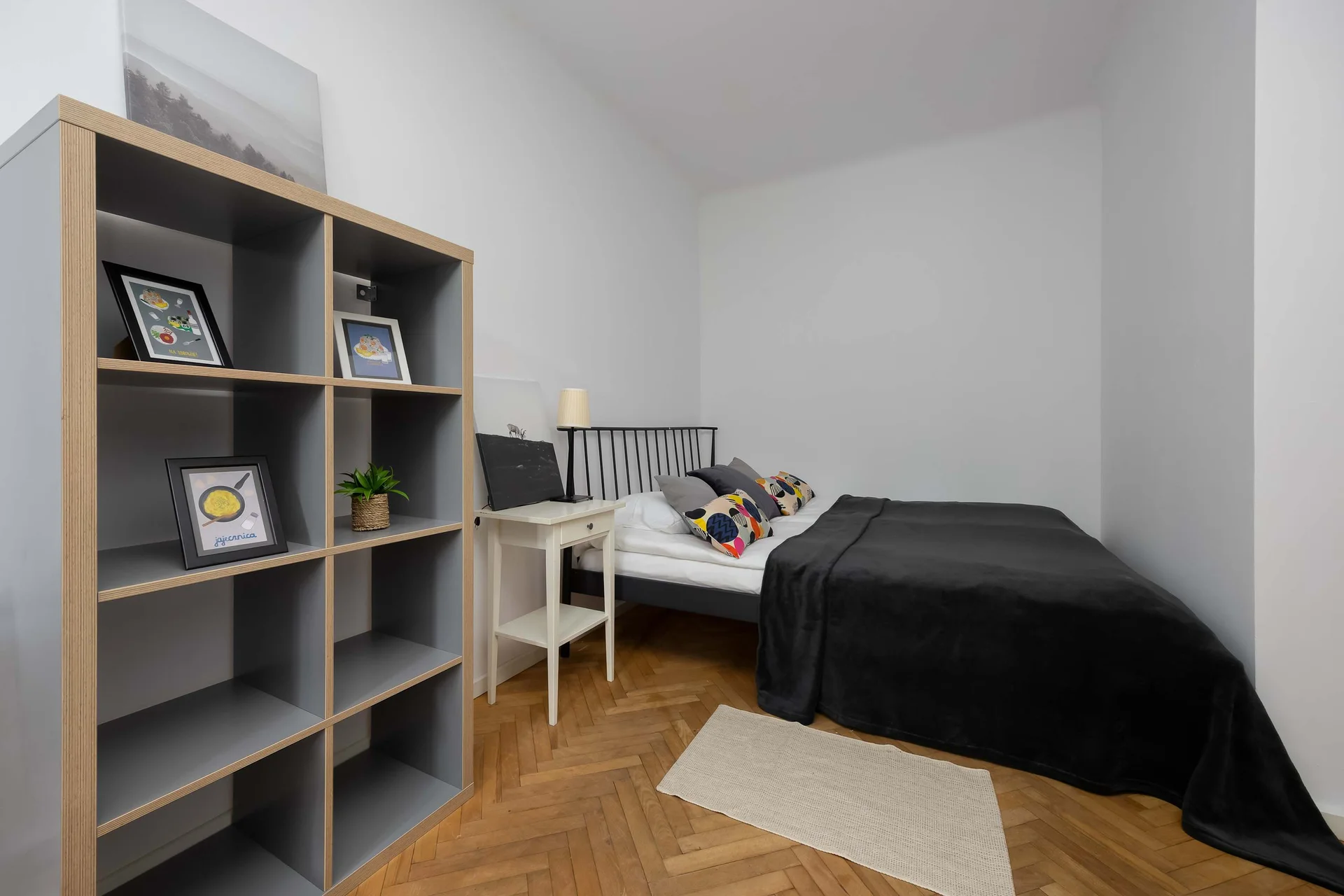 A cozy bedroom corner featuring a double bed with dark bedding and a gray shelving unit.