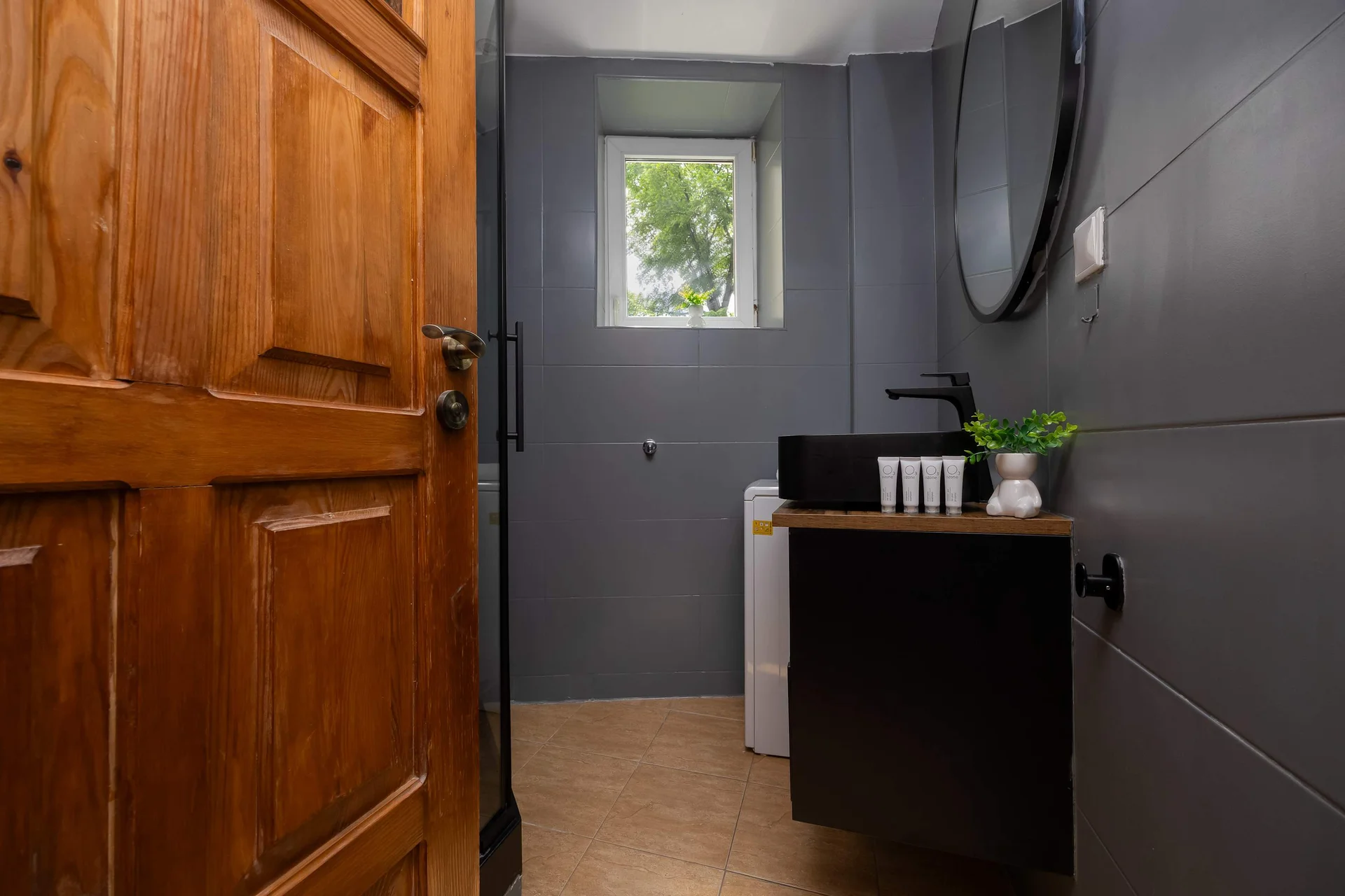 The bathroom featuring a dark tiled wall, vanity with sink, and mirror. The space is modern and well-organized.