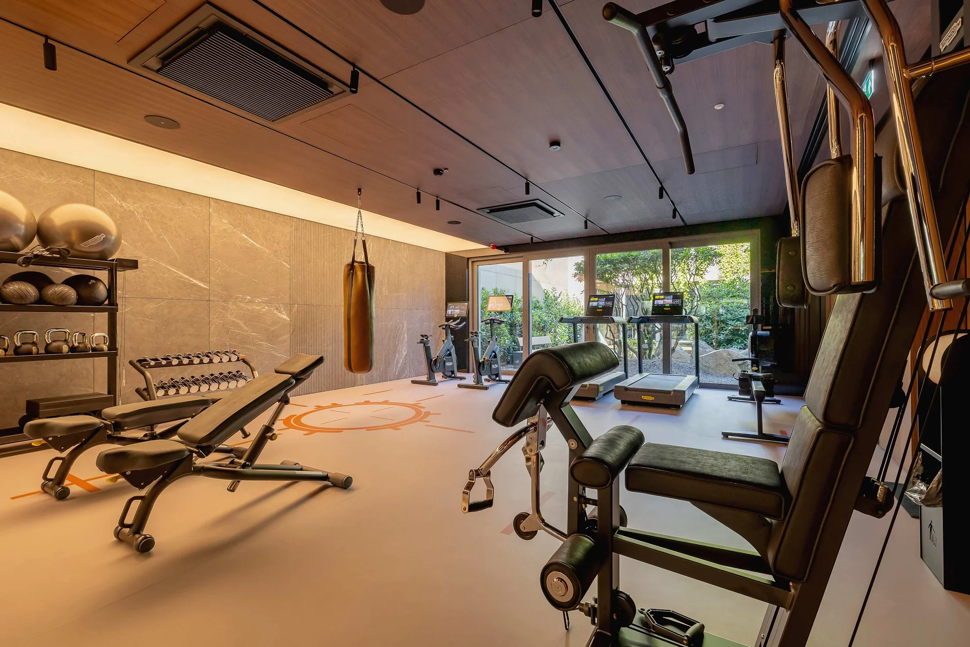 A modern gym area equipped with various workout machines, including benches and weights. Large windows allow natural light to brighten the space, making it feel open and motivating. The interior combines functionality with a contemporary design.