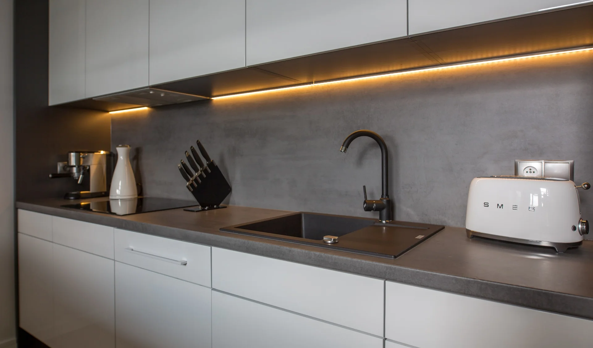The white, minimalist kitchen with elegant under-cabinet lighting makes cooking and enjoying meals together convenient.