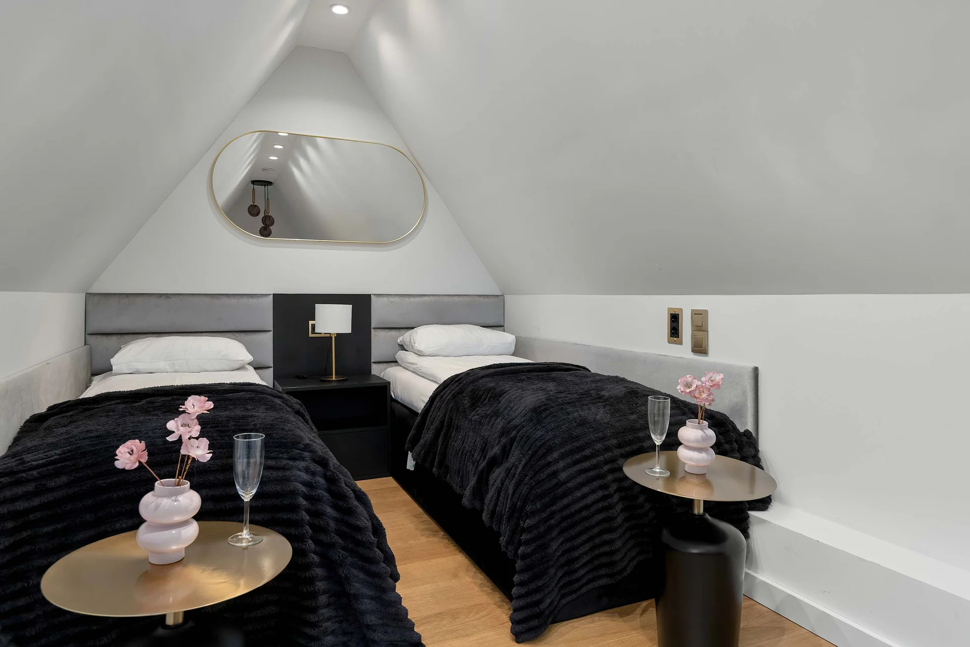 A cozy bedroom located under a slanted roof with two single beds pushed together. Black quilted bedspreads and small bedside tables add a stylish touch to the space.