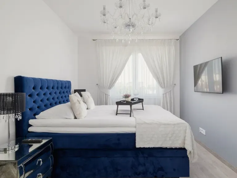 Eleganckie wnętrze apartamentu, granatowe łoże, biała pościel, białe ściany, TV