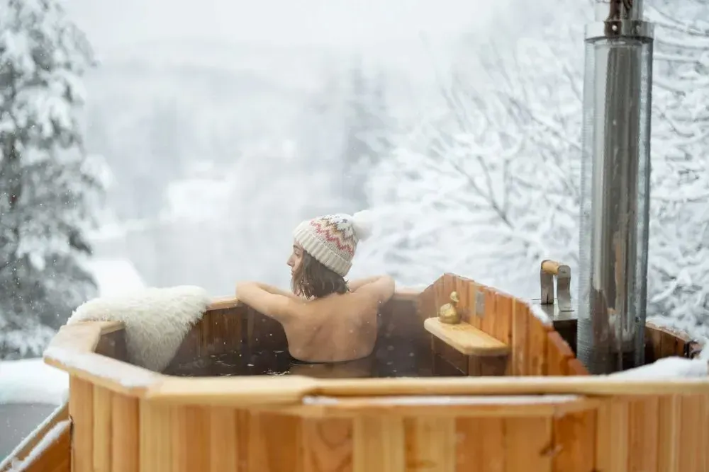 Kobieta w czapce, jacuzzi w górach w zimie, widokiem na naturę.
